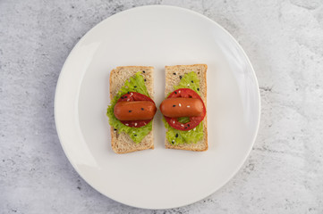 Sausage with tomatoes, salad and two sets of bread on a white plate.