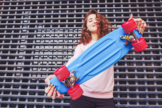 Contrast and vivid image of a young girl who holds out a nice skateboard in the direction of the camera