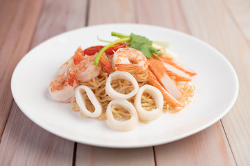 Stir-fried instant noodle with prawn and crab stick along  in a white dish.