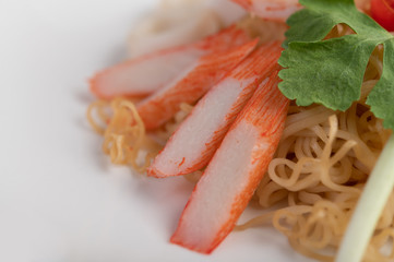 Stir-fried instant noodle with prawn and crab stick along  in a white dish.