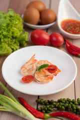 Three fresh shrimp and half tomatoes in a white plate on a wooden.
