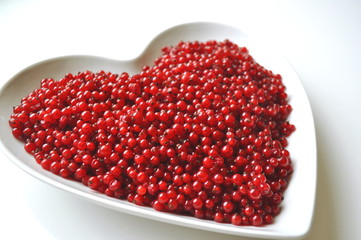 Fresh washed red currants berries in a heart shaped bowl on white with copy space