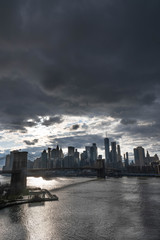 Manhattan skyline with Brooklyn bridge. Sky-rise skyscrapers tall apartment buildings. Dramatic cloudy sky with sun rays. 