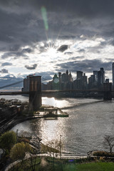 Manhattan skyline with Brooklyn bridge. Sky-rise skyscrapers tall apartment buildings. Dramatic cloudy sky with sun rays. 