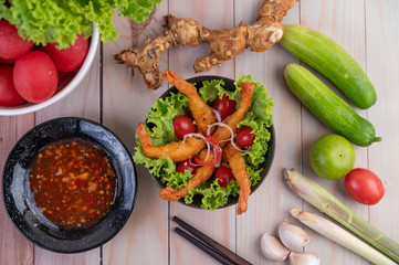 Shrimp deep fried batter placed on salad and tomatoes in a wooden bowl.