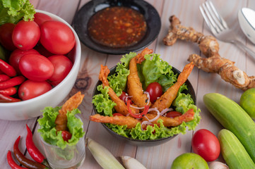 Shrimp deep fried batter placed on salad and tomatoes in a wooden bowl.