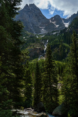 Grand mountains Grand Tetons in Wyoming. Mountain landscape with spring waters and mountain lakes. Blue sky. White clouds. Deep forest woods. 