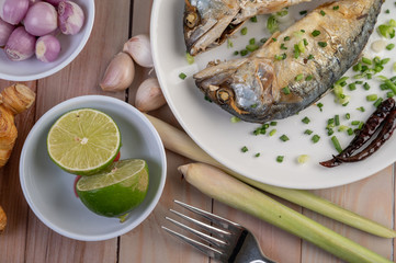 Two cooked mackerel, placed in a white dish, sprinkled with spring onions.