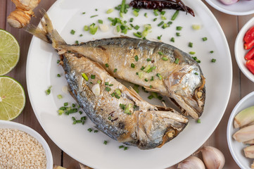 Two cooked mackerel, placed in a white dish, sprinkled with spring onions.