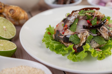 Deep-fried mackerel topped with galangal, pepper, mint, red onion in a white dish.