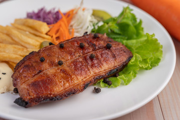 Fish steak with french fries, kiwi, lettuce, carrots, tomatoes, and cabbage in a white dish.