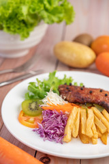 Fish steak with french fries, kiwi, lettuce, carrots, tomatoes, and cabbage in a white dish.