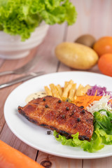 Fish steak with french fries, kiwi, lettuce, carrots, tomatoes, and cabbage in a white dish.