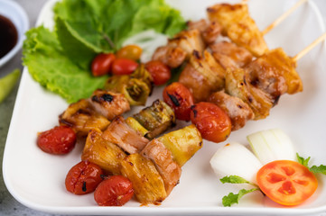 BBQ with a variety of meats, complete with tomatoes and bell peppers on a white plate.