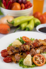 BBQ with a variety of meats, complete with tomatoes and bell peppers on a white plate.