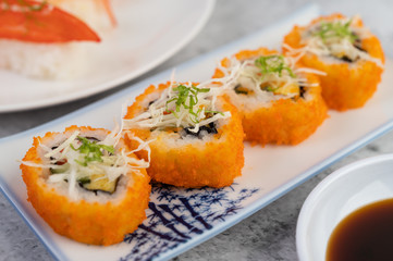 Sushi is on a plate with dipping sauce on a white cement floor.