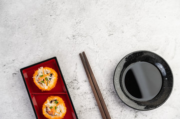 Sushi is in a plate with chopsticks and dipping sauce on a white cement floor.