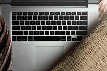 A laptop surrounded by bedding. 