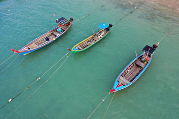 Fototapeta na wymiar Traditional Asian longtail fishing boats moored beside a sandy beach with palm trees 