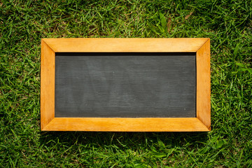 Empty chalk board on green grass background. Blank blackboard with wooden frame.