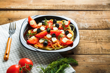 Black plate with spaghetti in a sauce with cherry tomatoes olives and mozzarella on a napkin with a fork.