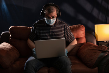 Middle aged man working at home on his computer for the coronavirus using protective equipment such as gloves and mask