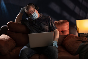 Middle aged man working at home on his computer for the coronavirus using protective equipment such as gloves and mask