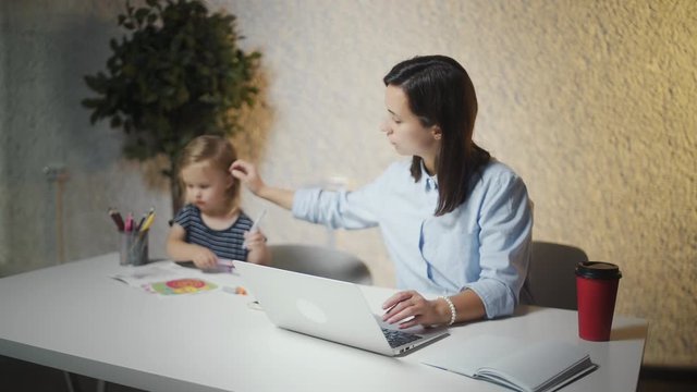 Young mother working on laptop while her child painting near to her