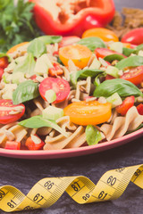 Tape measure and fresh salad with wholegrain pasta and vegetables. Healthy lifestyles and nutrition