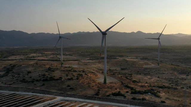 Windmill and Solar panel produces green, environmentaly friendly energy from the setting sun. View from drone. Landscape picture of a solar plant that is located inside a valley, Ninh Thuan, Vietnam