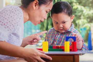 Mother as teacher with Little boy intend to building tower by wooden colorful block. Educational toys and home learning children concept. Selected focus