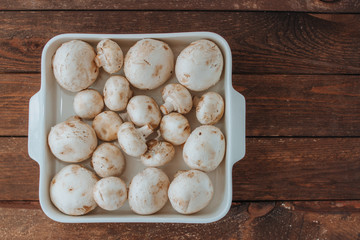 champignons in a white baking dish on a wooden background, free space