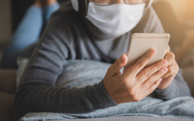 Young woman wearing mask staying at home listening music with smartphone, headphone relaxing emotion. Prevent the spread of coronavirus quarantine.