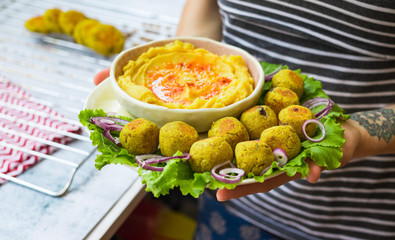 Woman hands hold baked chickpea falafel to eat with hummus, salad leaves and pita bread. Vegan healthy food. 