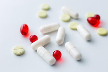 Multi-colored assorted tablets and capsules spilled out of a white table. White background. Copy space
