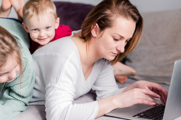 Young women works at home with laptop along with two children.Children want to communicate with mother, make noise and interfere with work.Self-isolation during coronovirus pandemic