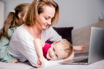 Young women works at home with laptop along with two children.Children want to communicate with...