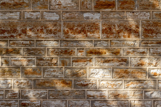 Abstract texture background of a 19th Century brown color natural limestone wall, with tuckpointing mortar restoration, showing filtered tree shadows from low angle sunlight