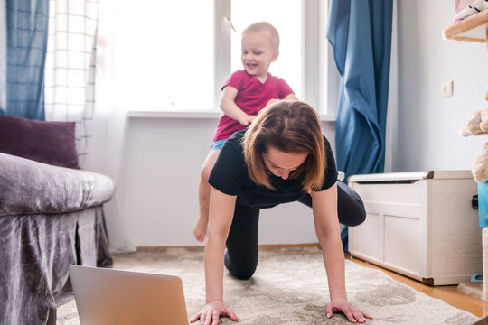 Beautiful Young Woman In A Black Tracksuit Doing Workout Exercises At Home Watching Videos On Her Laptop But The Child Prevents Her From Doing