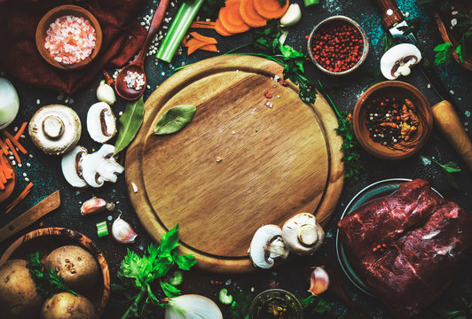 Food cooking background. Fresh organic vegetables, ingredients, spices and meat for warm autumn soup on vintage kitchen table with rustic wooden cutting board. Top view, place for text. 