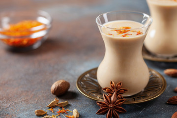 Golden Cinnamon Saffron Almonds Milk. Golden milk with species cardamom, turmeric, cinnamon, honey and ginger on wooden background. Trendy hot Healthy Vegan Drink. Indian Garam Badami Doodh.