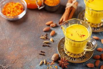 Golden Cinnamon Saffron Almonds Milk. Golden milk with species cardamom, turmeric, cinnamon, honey and ginger on wooden background. Trendy hot Healthy Vegan Drink. Indian Garam Badami Doodh.