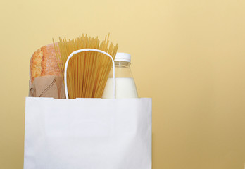 Donation food. Milk, bread, spaghtti in white bag on yellow background.