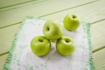 Ripe green apples on a green napkin lying on a canvas napkin and a wooden table surface. Background for fruits.