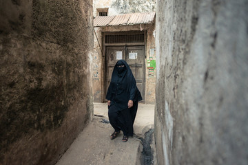 Portrait of adult Muslim woman wearing conservative niqab, only eyes visible, walking in narrow alley in Lamu island town