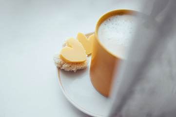 romantic homemade simple Breakfast sandwiches in the shape of a heart with cheese and a yellow mug with milk foam on the window.