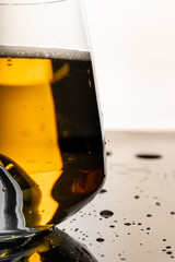 Full glass of nice gold colour fresh beer with air bubbles and white foam on black reflective surface with sprayed water drops on it
