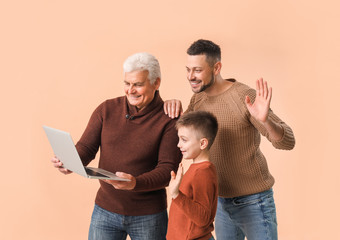 Man with his father and son using laptop on color background