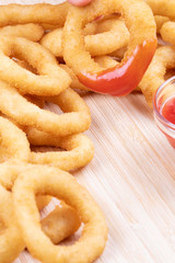 Delicious onion rings with ketchup on a wooden cutting board