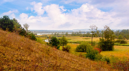 Fototapeta na wymiar Autumn landscape with sloping hill, trees by river in distance